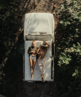 Two people lying on a vintage car in a forest setting