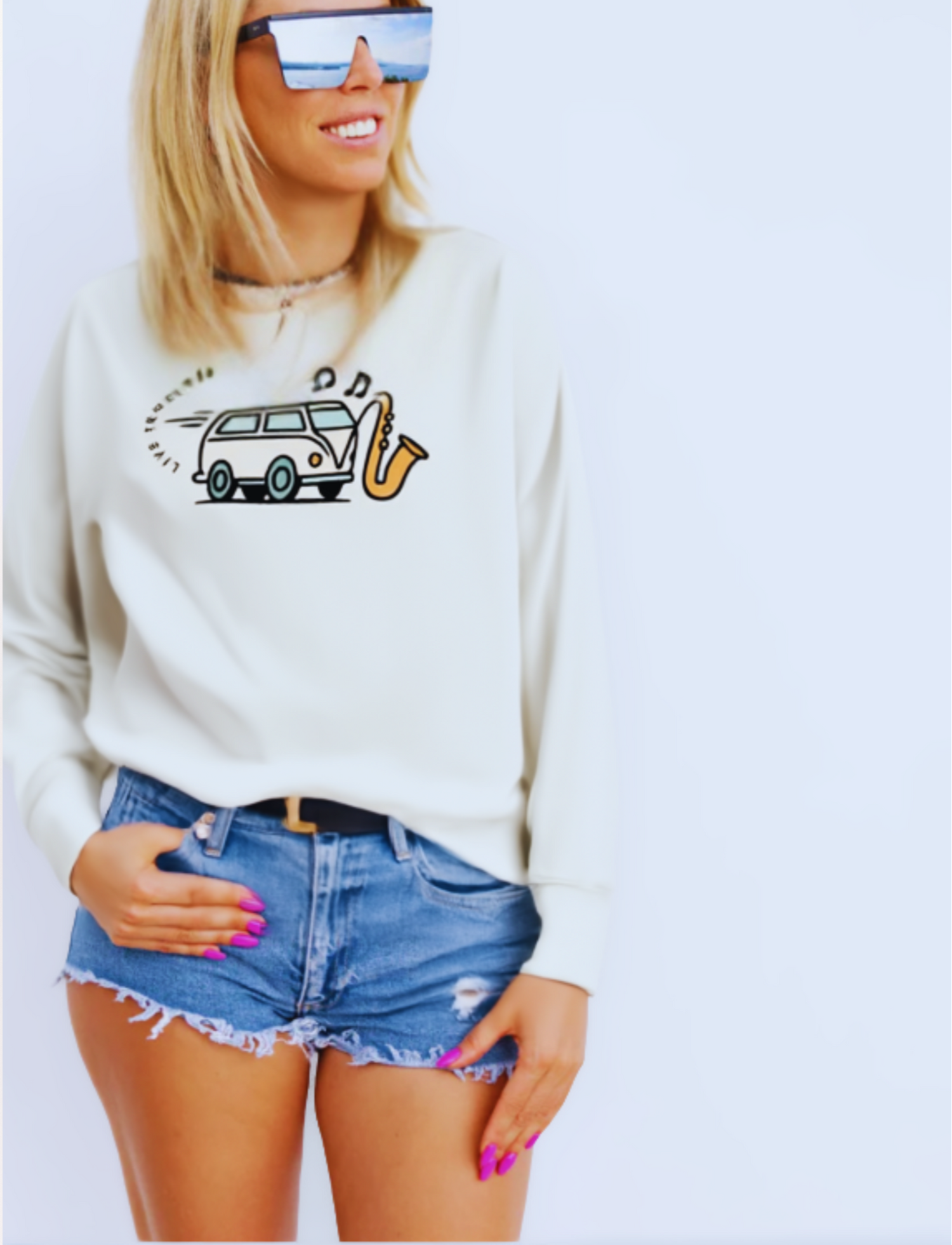 Person wearing a white sweatshirt with a graphic design and denim shorts on a plain background