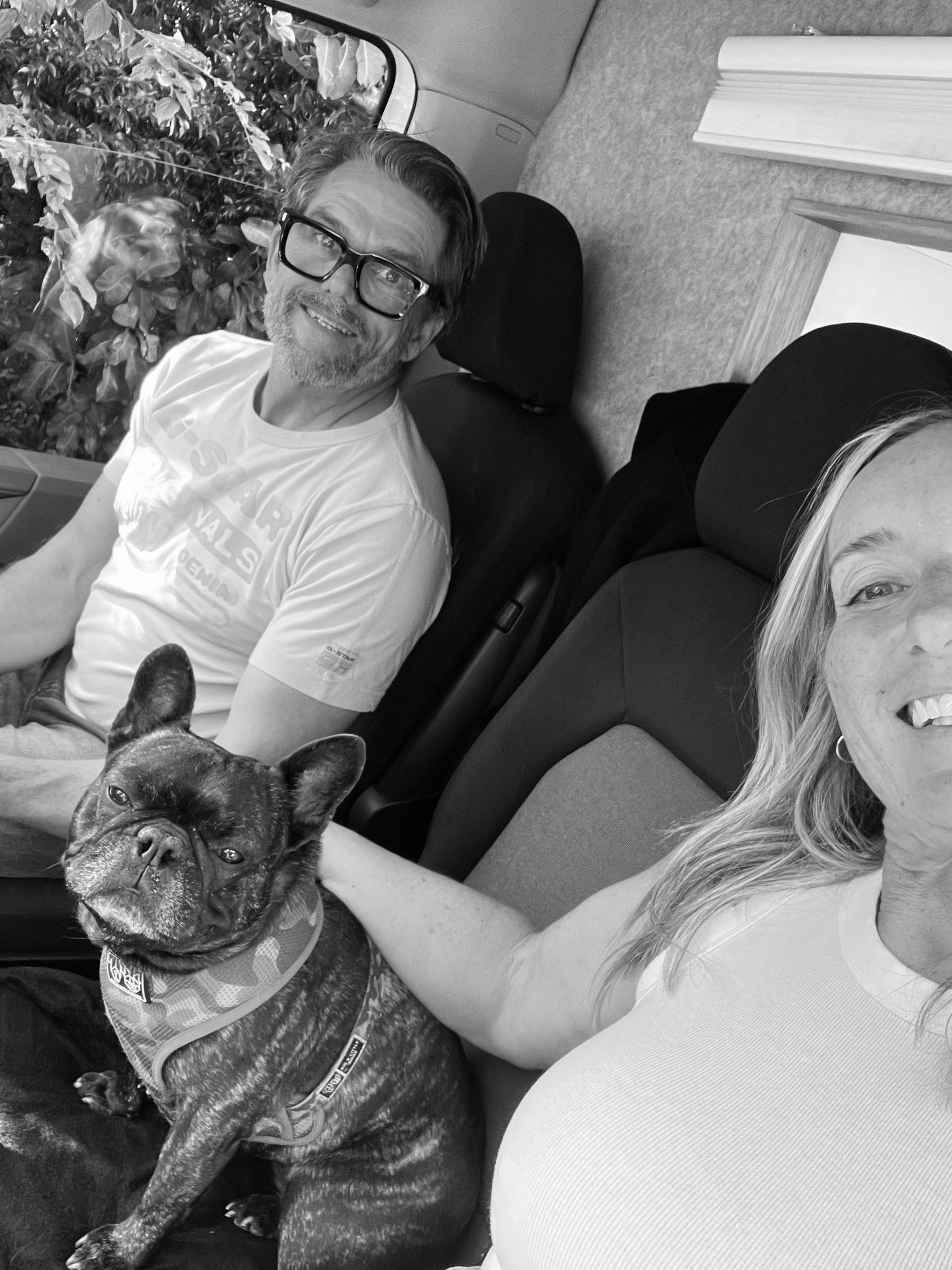 Two people sitting in a car with a dog, black and white photo